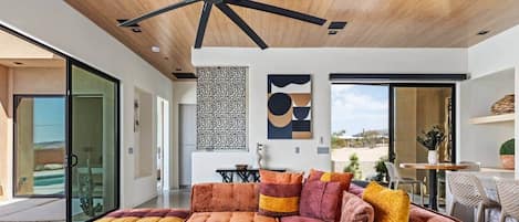 Una sala moderna con un sofá modular, un ventilador de techo de madera y un amplio ventanal con vistas al exterior.