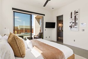 A modern hotel room with a large bed, a flat-screen TV, a sliding glass door to a balcony, and a view of the outside.
