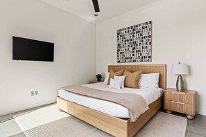 A modern bedroom with a wooden bed, a bedside table with a lamp, and a wall-mounted TV. - Nightfall | Custom pool, spa, sauna, & game room (Twentynine Palms)
