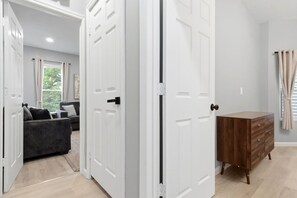 Une pièce avec une commode en bois, un canapé gris et une porte blanche.