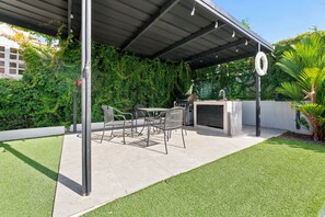 Eine Terrasse im Freien mit Grill, Sitzgelegenheiten und einem Wasserspiel.