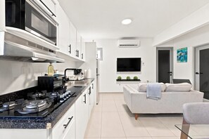 Une cuisine moderne équipée d’une cuisinière, d’un four à micro-ondes et d’un évier, un espace de vie avec un canapé et une télévision, et une porte ornée d’un tableau.