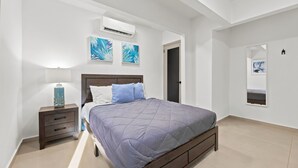 A bedroom with a bed, a nightstand, a lamp, and artwork on the walls. - Brisamare Apt 5 | 2BR | Pool, BBQ, Generator (San Juan)
