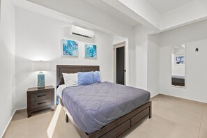 A bedroom with a bed, a nightstand, a lamp, and artwork on the walls. - Brisamare Apt 5 | 2BR | Pool, BBQ, Generator (San Juan)