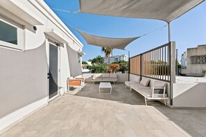 Une terrasse sur le toit, aménagée avec du mobilier d’extérieur, dotée d’un grand auvent et offrant une vue sur le paysage urbain.