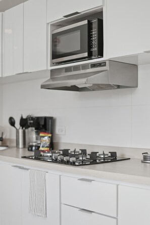 Ett kök med en mikrovågsugn i rostfritt stål, en gasspis och vita skåp.