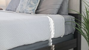 Ein Bett mit hölzernem Kopfteil, ein großes abstraktes Gemälde darüber und eine Zimmerpflanze seitlich.