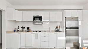 Eine moderne Küche mit weißen Schränken, einem Edelstahlkühlschrank, einer Mikrowelle und einer Kaffeemaschine.