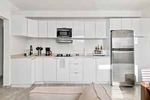 Eine moderne Küche mit weißen Schränken, einem Edelstahlkühlschrank, einer Mikrowelle und einer Kaffeemaschine.