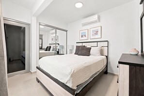 A modern bedroom with a large bed, a wardrobe, a mirror, and two framed pictures on the wall. - Brisamare Apt 4 | 1BR | Pool, BBQ, Generator (San Juan)
