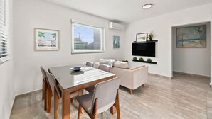 A modern living room with a dining area, a flat-screen TV mounted on the wall, and artwork on the walls. - Brisamare Collection | Pool | Sleeps 14 (San Juan)