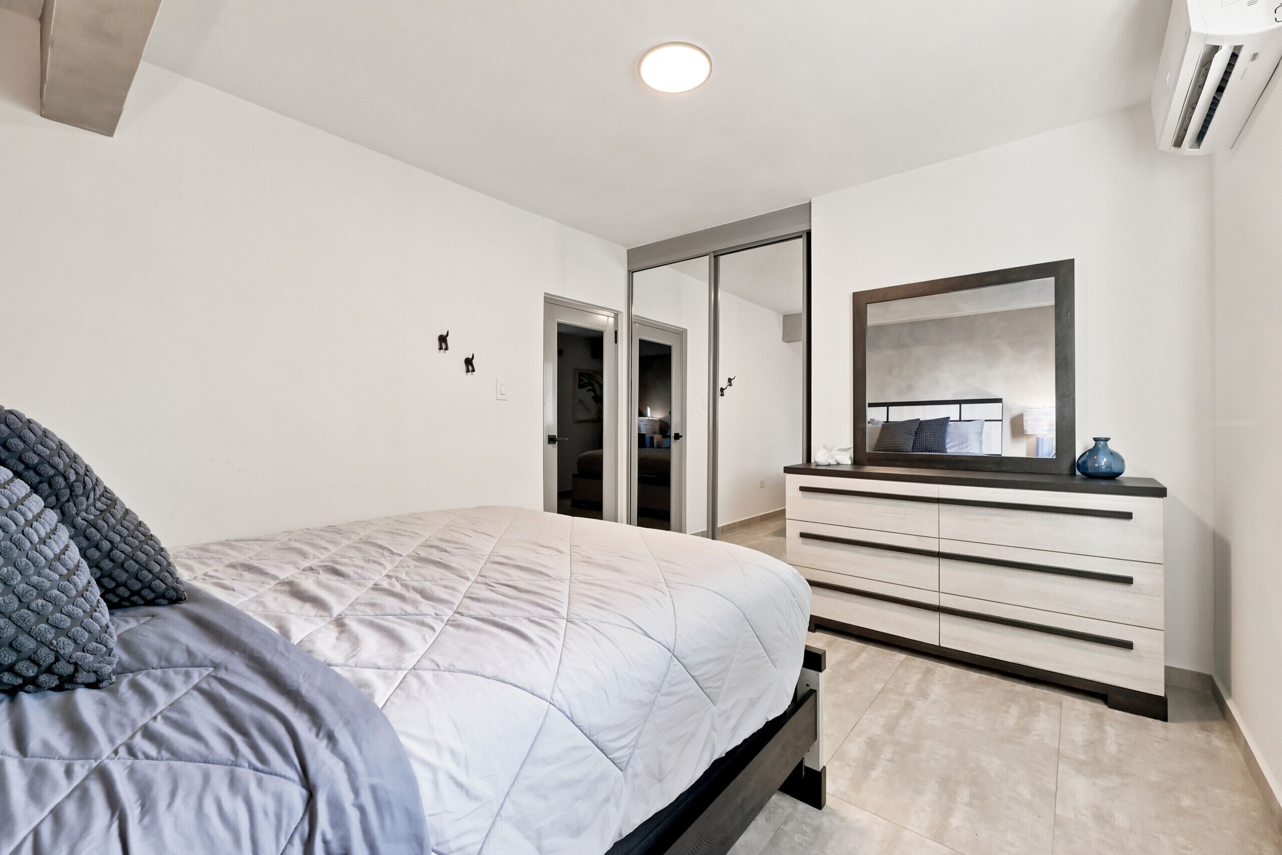Une chambre à coucher moderne, avec un lit, une commode, un miroir et une porte donnant sur un placard.