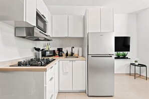 Eine moderne Küche mit weißen Schränken, einem Edelstahlkühlschrank, einer Mikrowelle und einem Gasherd.