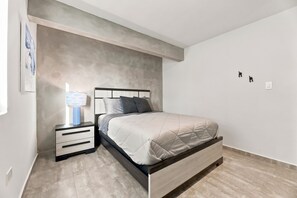 A bedroom with a bed, bedside tables, a lamp, and a wall-mounted light switch. - Brisamare Apt 2 | 2BR | Pool, BBQ, Generator (San Juan)