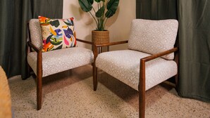Une pièce d’angle avec deux fauteuils, une plante en pot et des rideaux foncés.