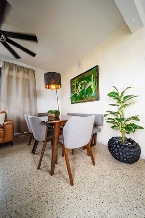 A dining area with a table and chairs, a ceiling fan, a wall-mounted painting, and a potted plant.