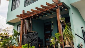 Un bâtiment à deux étages, à la façade bleu clair, avec une pergola en bois au rez-de-chaussée et un escalier menant à l’entrée.