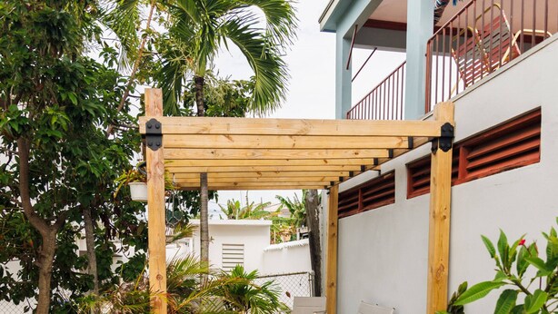 Un patio abrité agrémenté d’une pergola en bois, de meubles d’extérieur et de diverses plantes.