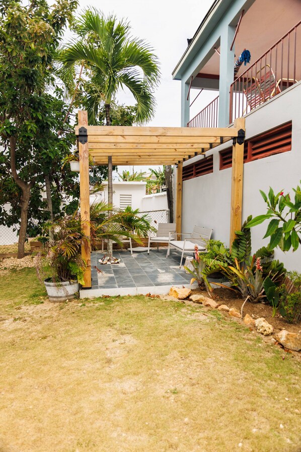 A covered patio area with a wooden pergola, outdoor seating, and a variety of plants.