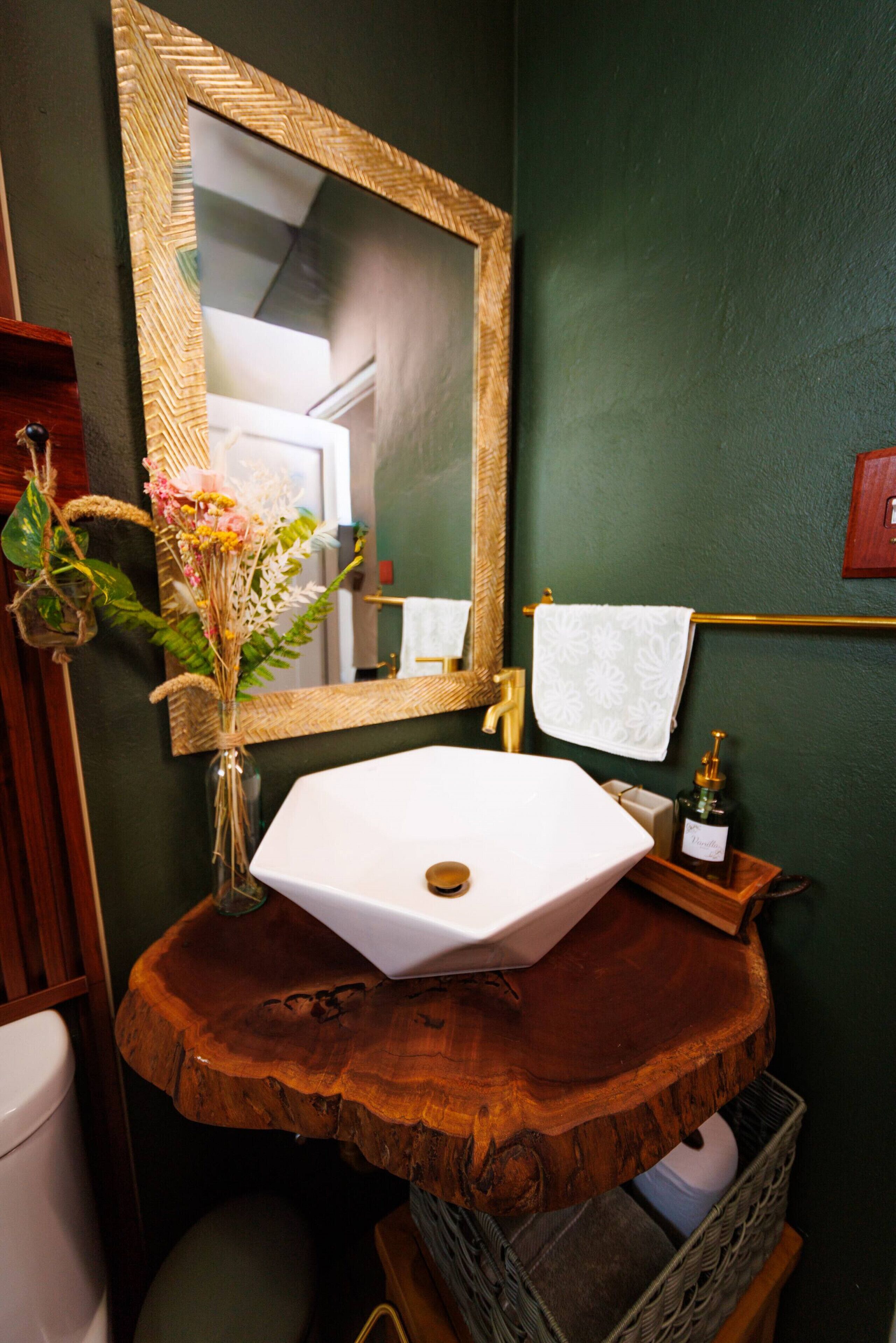 Un tocador de baño con un lavabo blanco, un espejo y un florero con flores.
