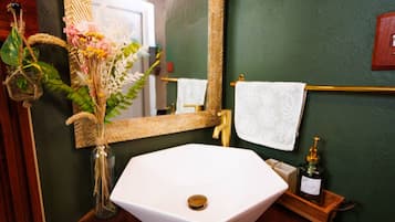 Un tocador de baño con un lavabo blanco, un espejo y un florero con flores.
