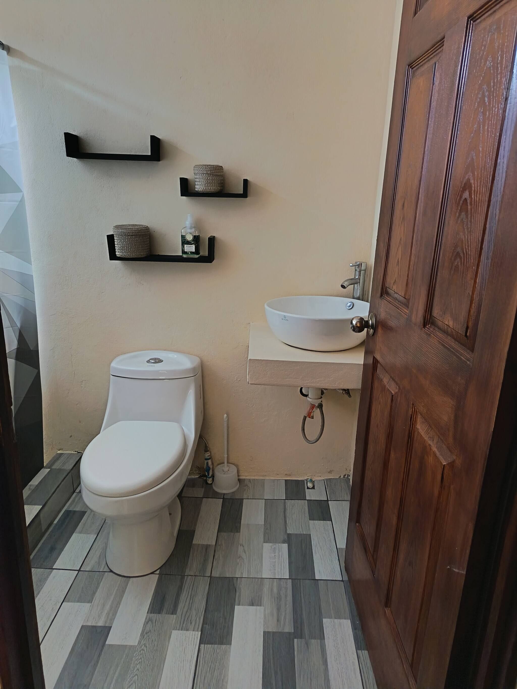 A bathroom with a toilet, a sink, and two shelves with containers.