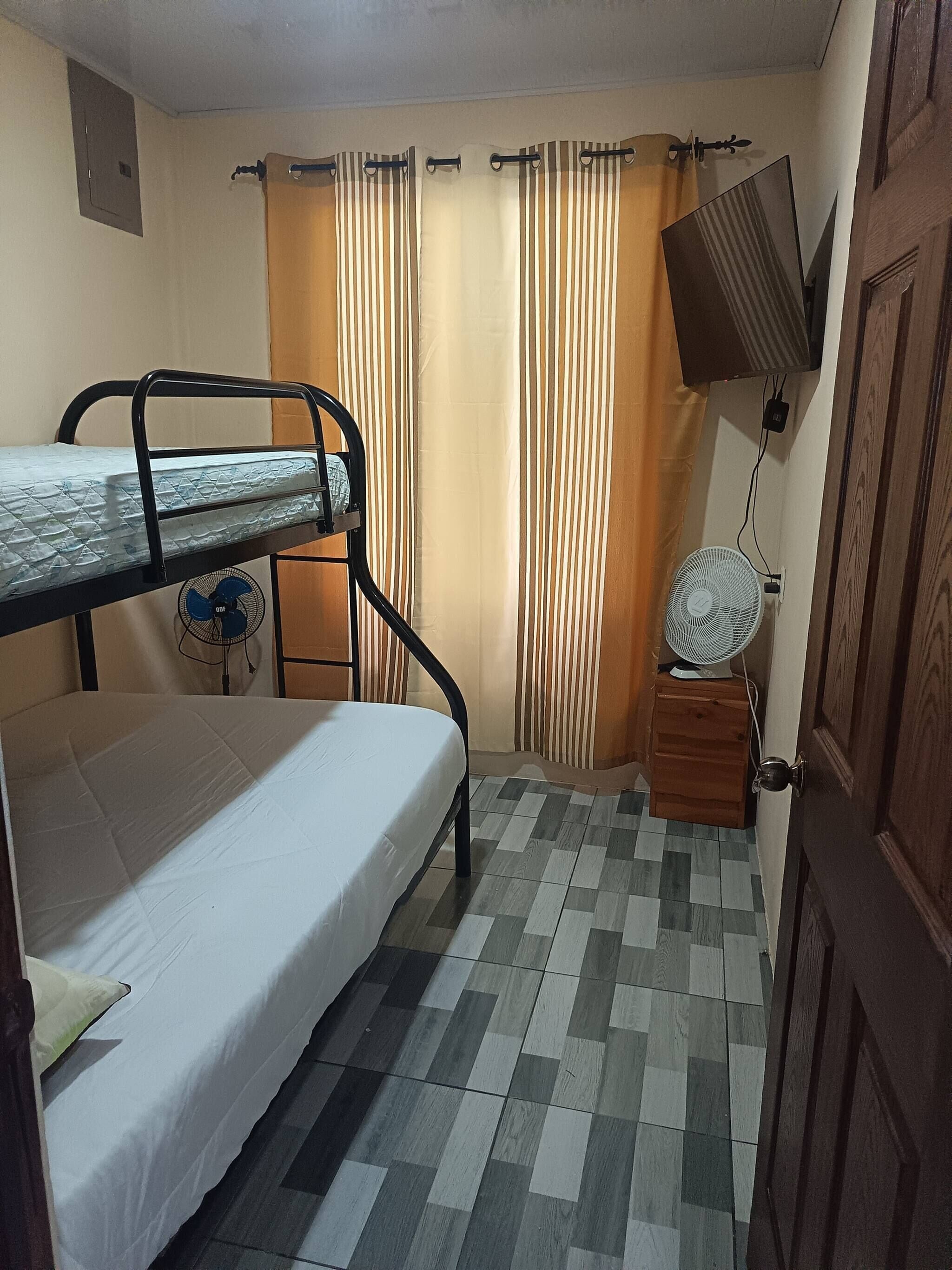 A room with a bunk bed, a small fan, a television, and a door.