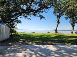 A lakeside property with a wooden shed, a concrete path, and a bench overlooking the water.