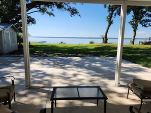 Un patio techado con una mesa de vidrio, sillas y vista a un lago.