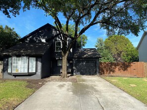 A residential house with a garage, a driveway, and a large tree in the front yard. - Spacious 4-bedroom Monthly Stay Cozy house with AC in terrific Arlington TX (Arlington)