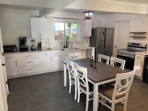 A modern kitchen with white cabinetry, a dining table with chairs, a refrigerator, an oven, and a coffee maker. - Spacious 4-bedroom Monthly Stay Cozy house with AC in terrific Arlington TX (Arlington)