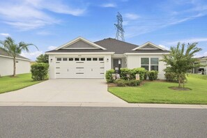 A single-story house with a garage, a well-maintained lawn, and a clear sky. - Spacious 3BR · Sleeps 7 · King Bed · Lanai (Okahumpka)