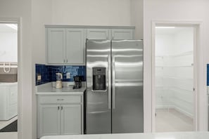 Eine moderne Küche mit weißen Schränken, einem Edelstahlkühlschrank, einer Kaffeemaschine und einem Wasserspender.