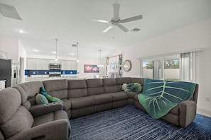 Ein modernes Wohnzimmer mit einem Ecksofa, einem Deckenventilator und Blick auf die Küche und den Essbereich.