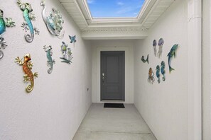A hallway with a skylight, a door at the end, and decorative wall art. - Spacious 3BR · Sleeps 7 · King Bed · Lanai (Okahumpka)