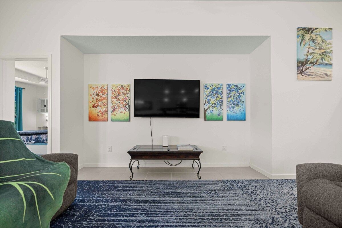 A living room with a flat-screen TV mounted on the wall, a coffee table, and a blue patterned rug.