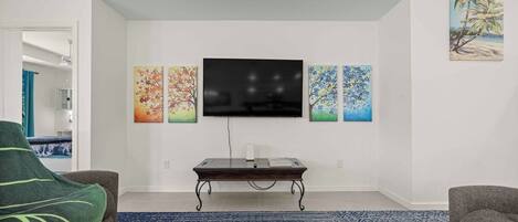 A living room with a flat-screen TV mounted on the wall, a coffee table, and a blue patterned rug.