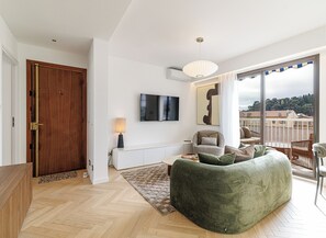 A modern living room with a sofa, a TV, and a balcony with a view. - Mamabaldi Apartment – Elegance, tranquility and views from the top of Nice (Nice)