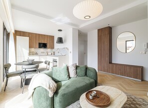 A modern living room with a green sofa, a dining area with a round table, and a kitchen with wooden cabinets. - Mamabaldi Apartment – Elegance, tranquility and views from the top of Nice (Nice)