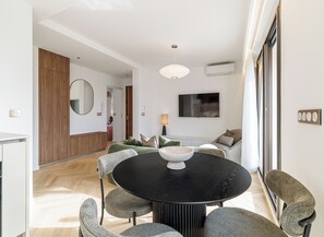 A modern living room with a round black table, grey upholstered chairs, a large mirror, and a flat-screen TV mounted on the wall. - Mamabaldi Apartment – Elegance, tranquility and views from the top of Nice (Nice)