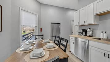 A modern kitchen with white cabinets, a stainless steel refrigerator, and a dining area with a wooden table set for four.