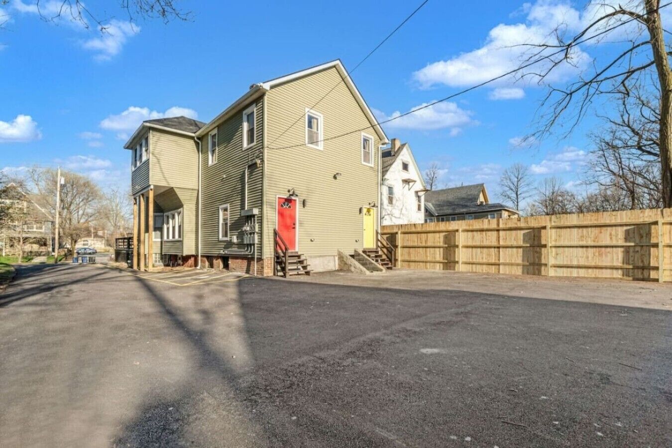 Une maison à deux étages avec un porche à l’avant, une porte rouge et une clôture en bois.