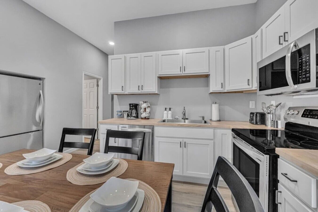 Una cucina moderna con pensili bianchi, un tavolo da pranzo in legno apparecchiato con piatti e un forno a microonde integrato.