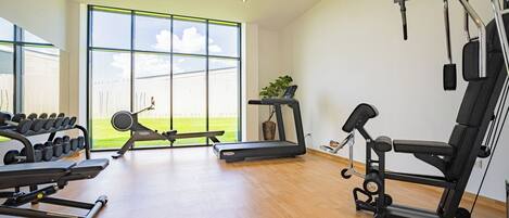 Un gimnasio moderno con diversos equipos de ejercicio, ventanas amplias y suelo de madera.