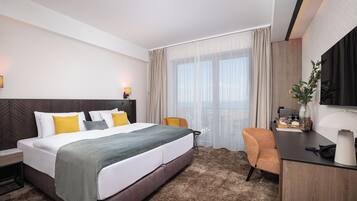 A hotel room with a large bed, a desk, a chair, and a TV.