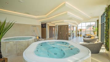 A modern indoor pool area with two hot tubs, a lounge area with seating, and a view of the city through large windows.