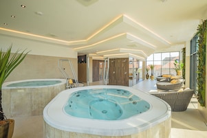 Un área de piscina interior moderna con dos jacuzzis, un espacio de relajación con asientos y vistas a la ciudad a través de amplias ventanas.