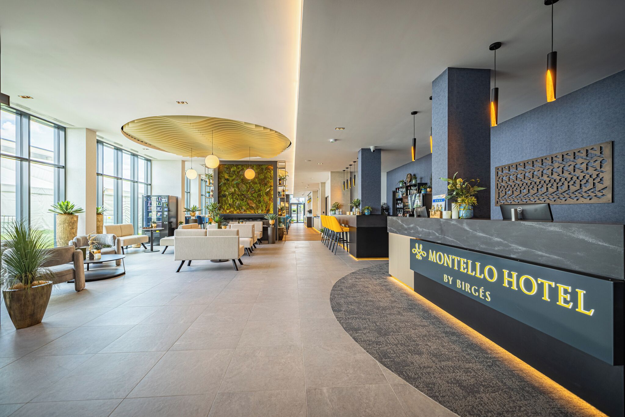 Un espace d’accueil d’hôtel au design moderne, comprenant un comptoir d’accueil, un coin salon et un grand mur orné d’un motif géométrique.