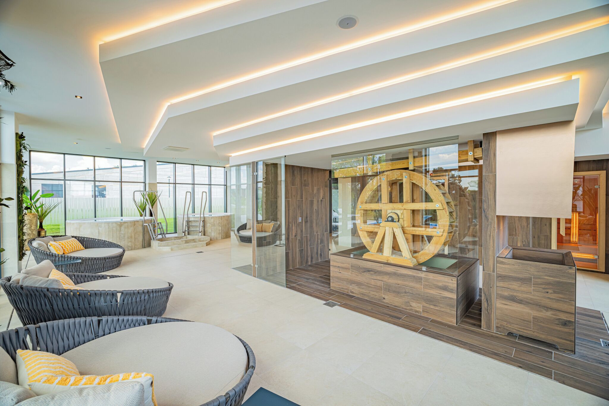 A spacious indoor area with modern furniture, a large wooden wheel structure, and a glass partition.