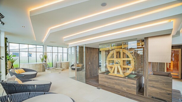 A spacious indoor area with modern furniture, a large wooden wheel structure, and a glass partition. - Montello Hotel (Balatonfüred)